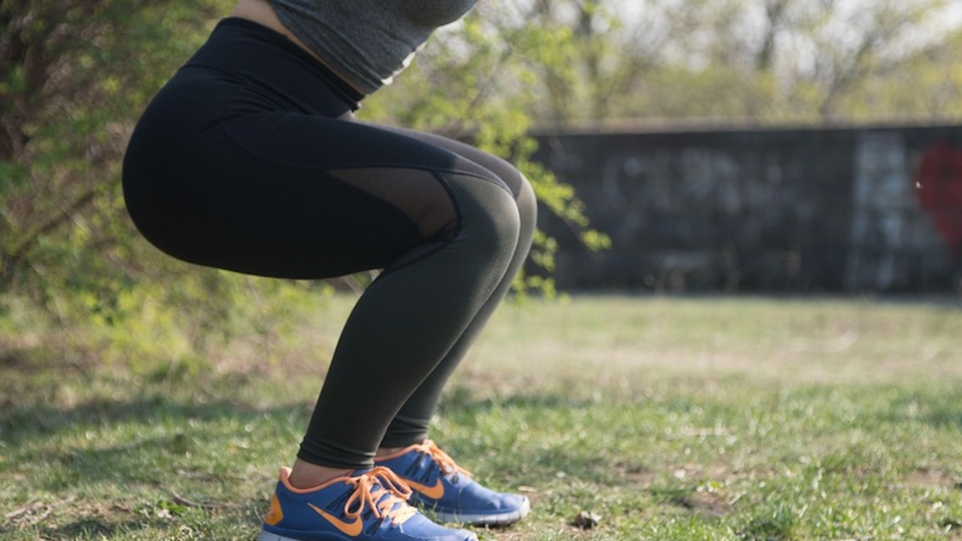 The legs and torso of a person in black leggings doing a squat outside