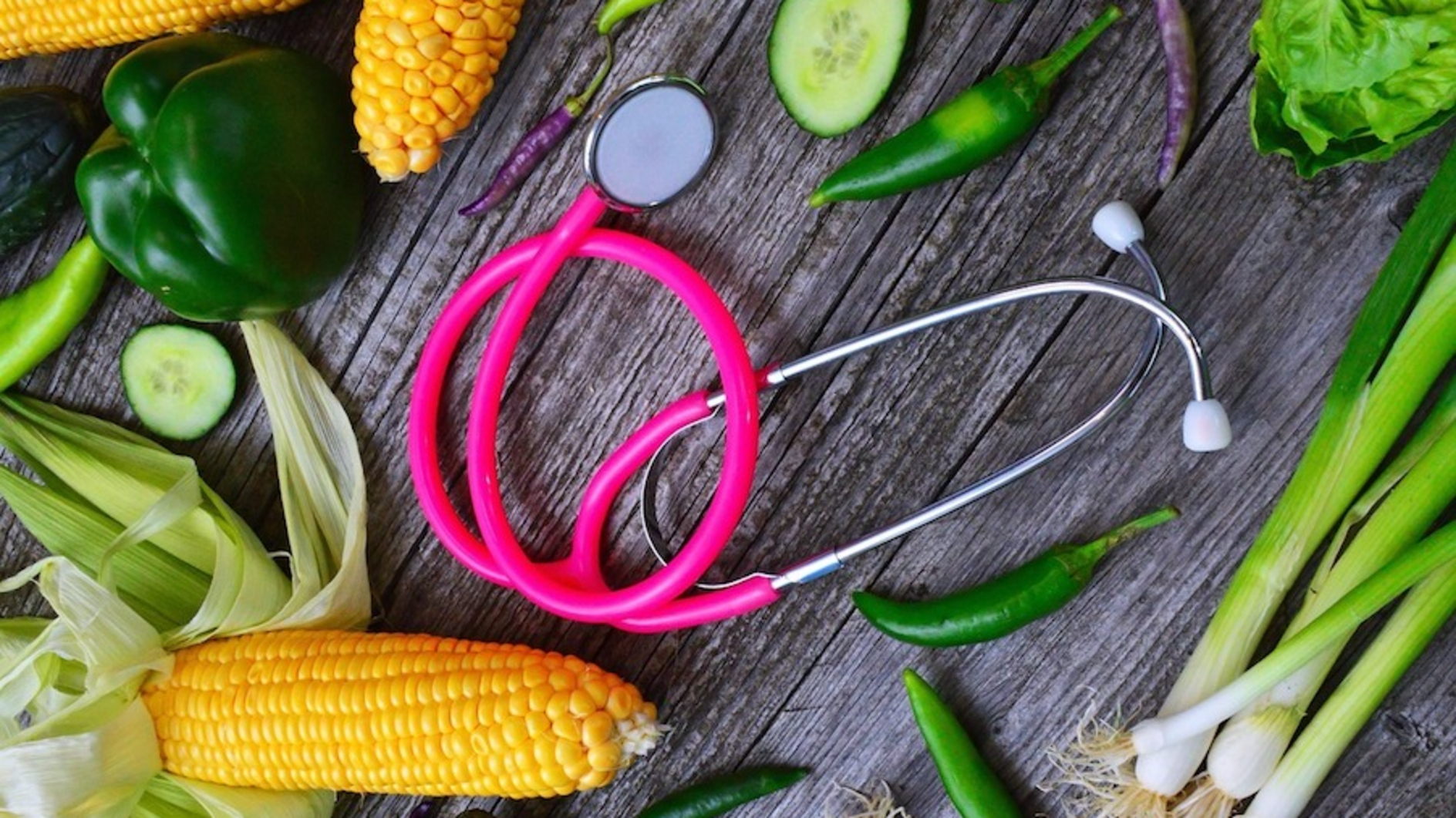 A pink stethoscope surrounded by vegetables