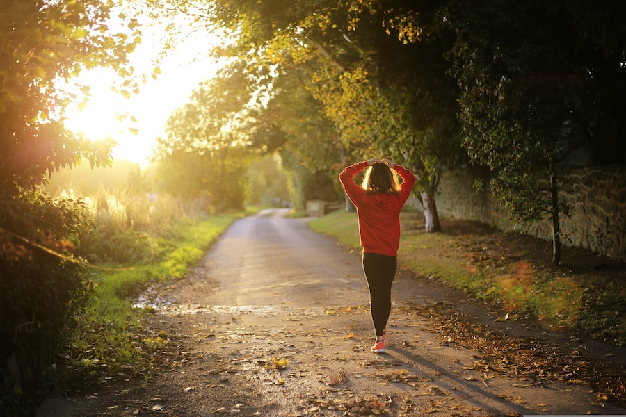 A person in an orange jacket walking down a tree-lined road at sunset