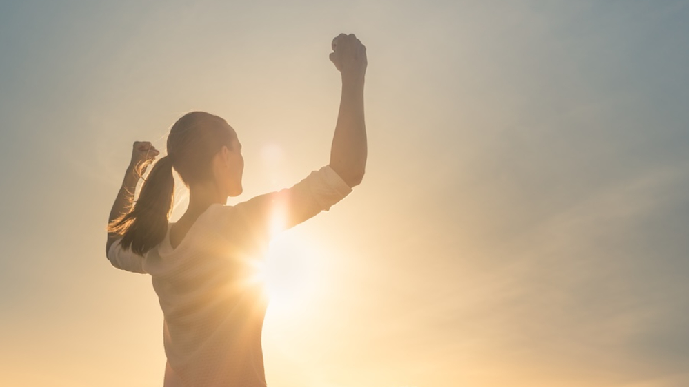 A woman raising her fists, backlit by the sunrise